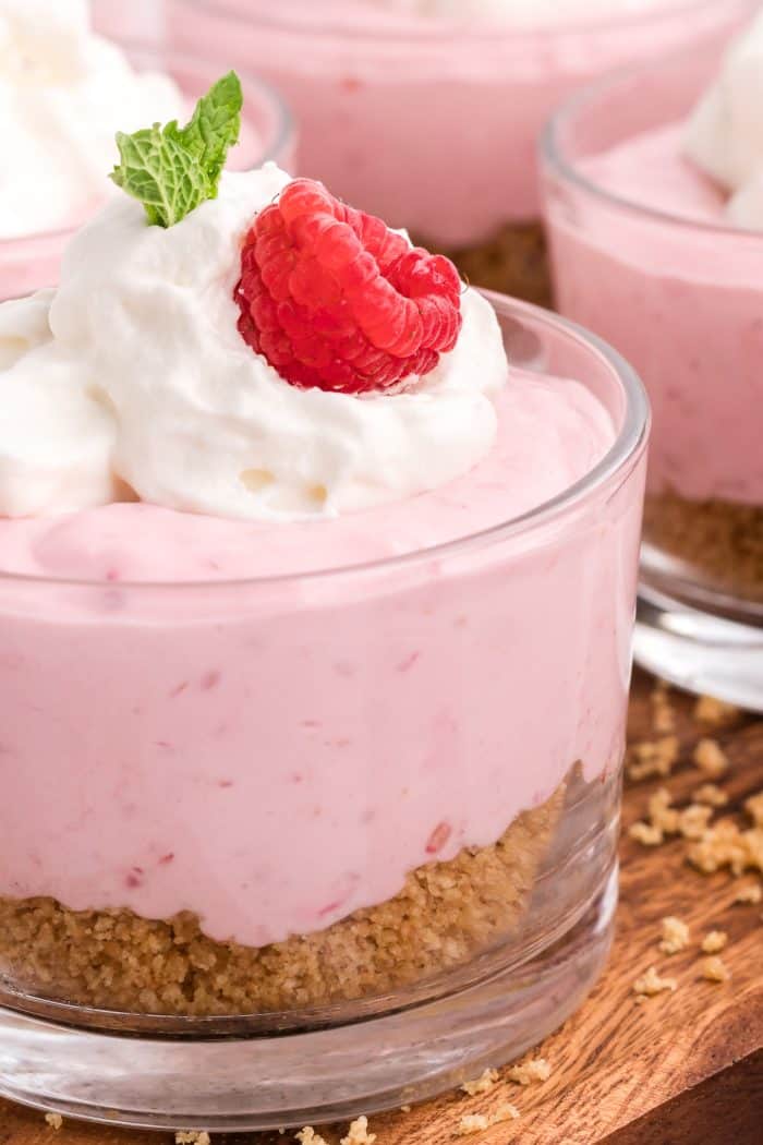 A closeup of raspberry mousse garnished with a fresh raspberry, mint leaf, and whipped cream.