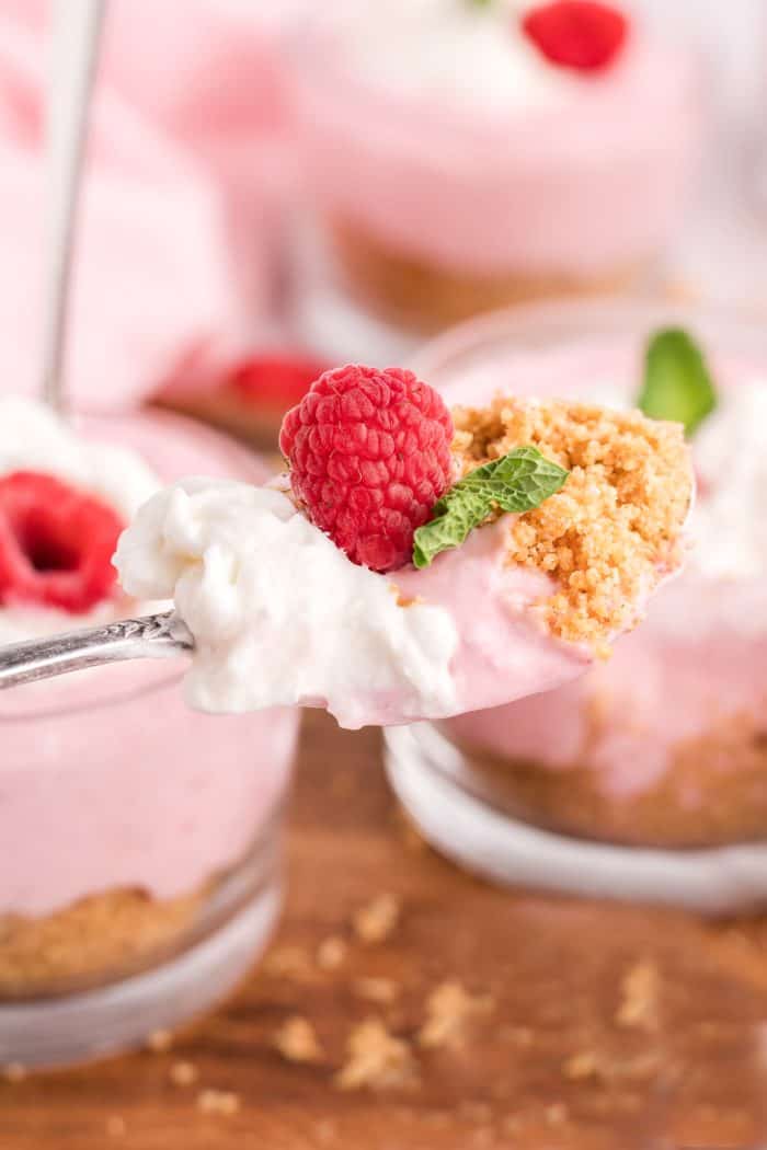 A glass serving dish with raspberry mousse and a spoon with a scoop of all the layers of the raspberry mousse. 
