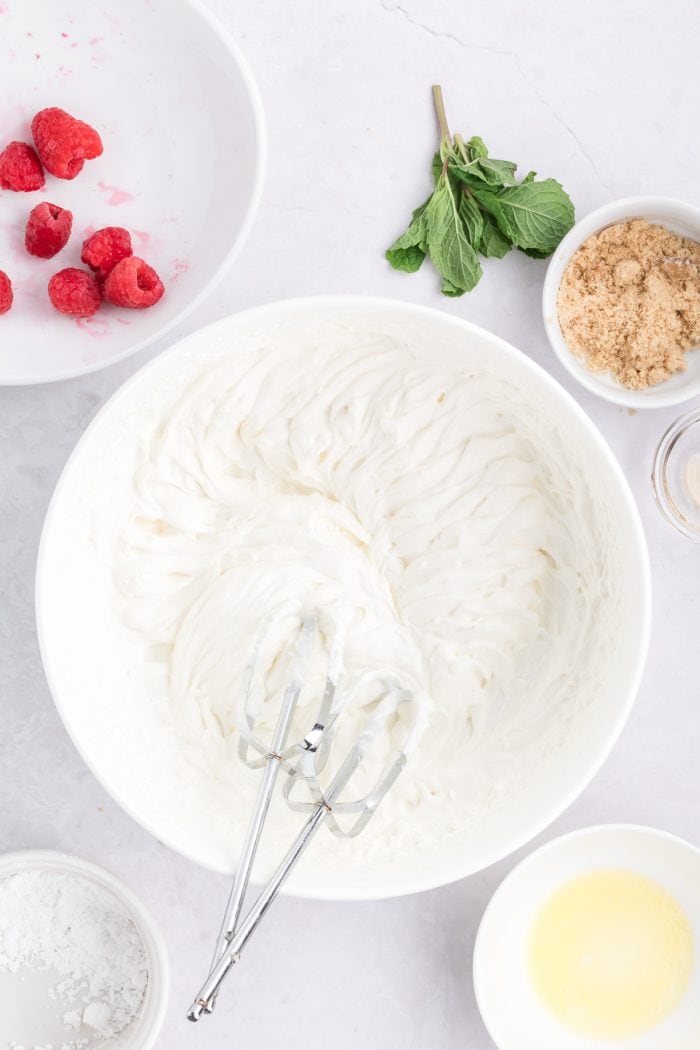 Whipping cream, whipped to soft peaks with a hand mixer in a white bowl.