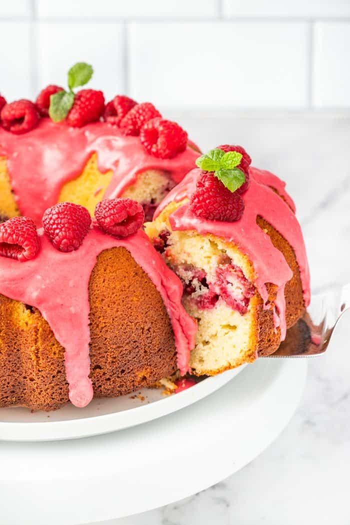 A lemon raspberry bundt cake with a slice being removed.