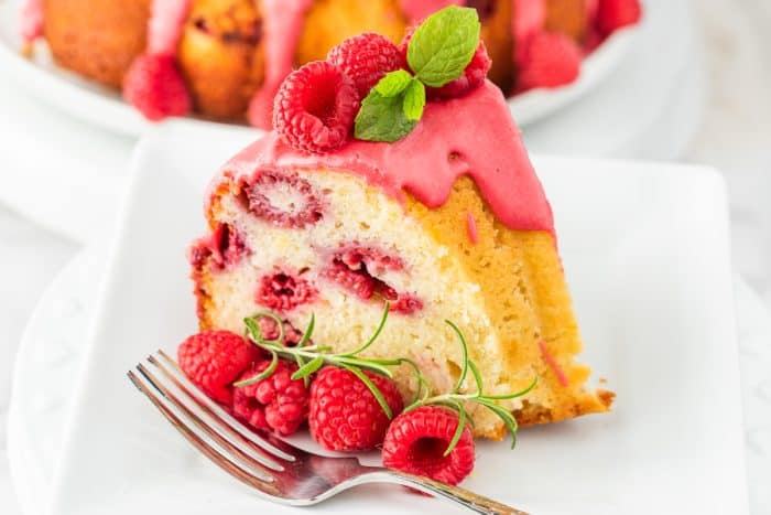 A slice of lemon raspberry bundt cake on a white plate with a fork. 