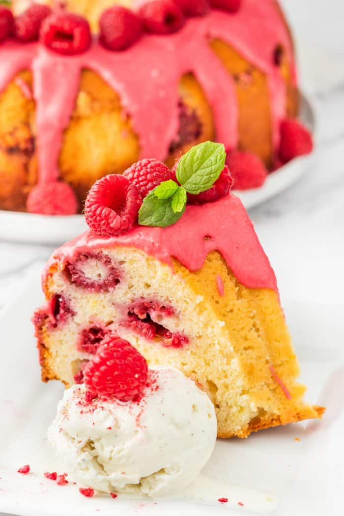 A slice of lemon raspberry bundt cake with a scoop of ice cream on a white plate.
