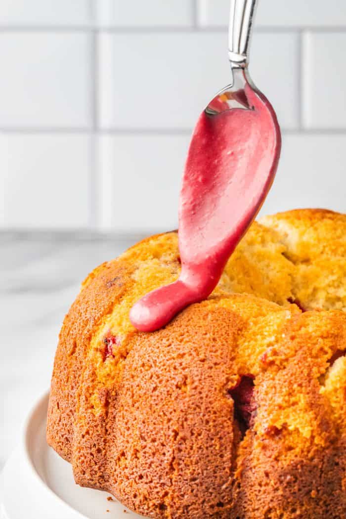 A bundt cake with raspberry icing being dripped over it. 