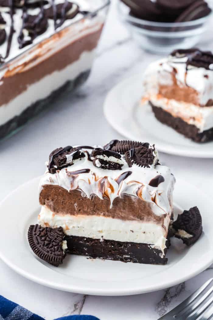 Two plates with slices of no bake Oreo layered dessert with the glass dish with the dessert in it in the background.