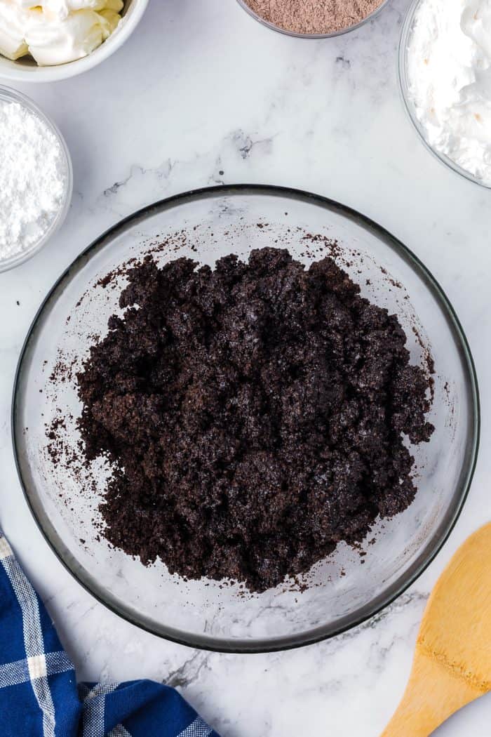 Oreo crumbs mixed with melted butter in a glass bowl.