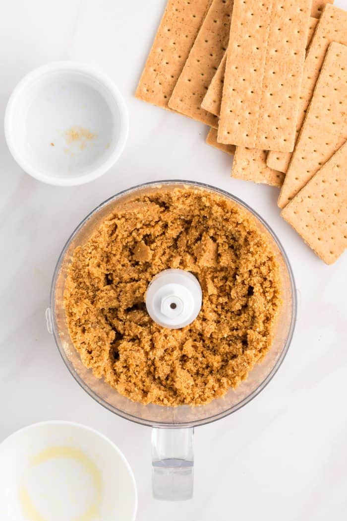 A food processor with graham cracker crumbs mixed with butter.