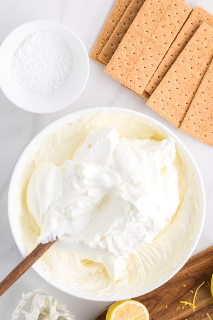 Whipping cream added to a white bowl with graham crackers in the background.