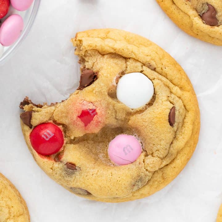 A close up of a Valentine's M&M cookie with a bite out of it and cookies around it.
