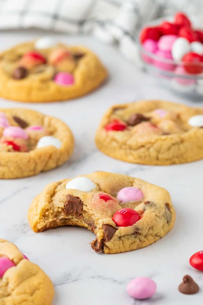 An overview of four cookies with Valentine's M&M's. One cookie has a bite out of it.