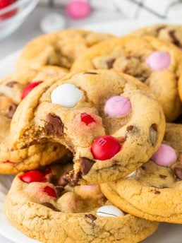 A pile of Valentine's M&M Cookies with one cookie with a bite out of it.