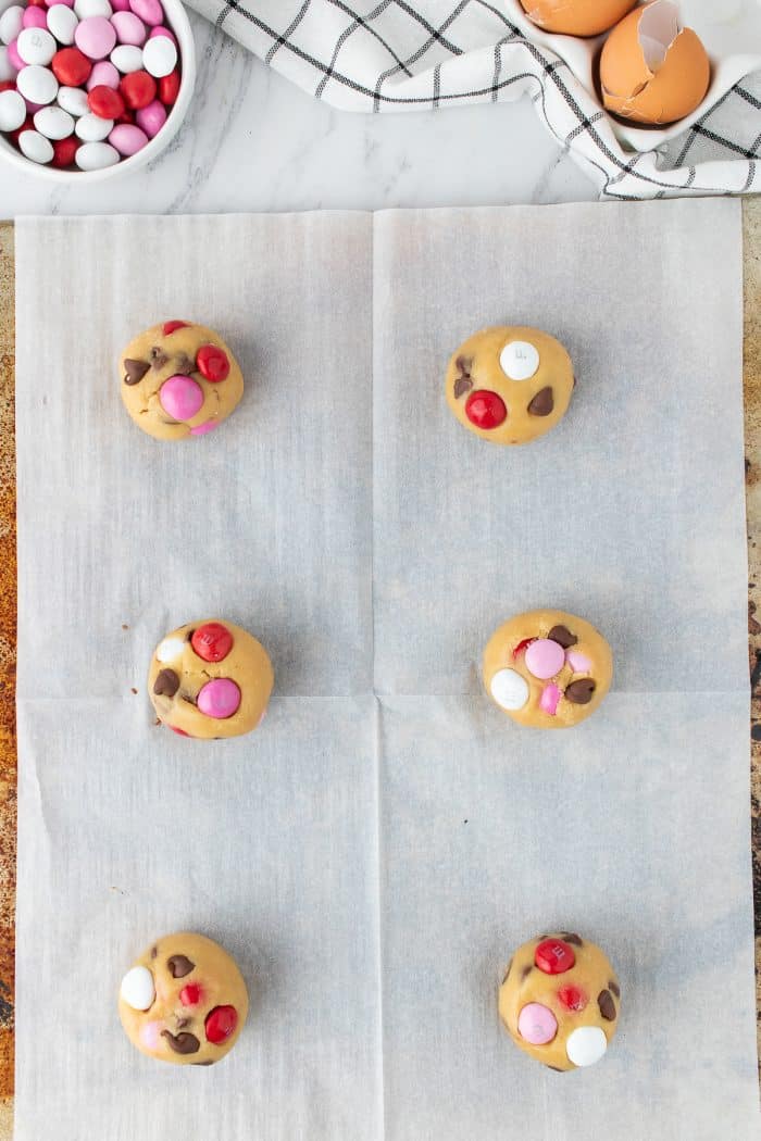 A baking sheet with balls of cookie dough with M&M pressed into them.
