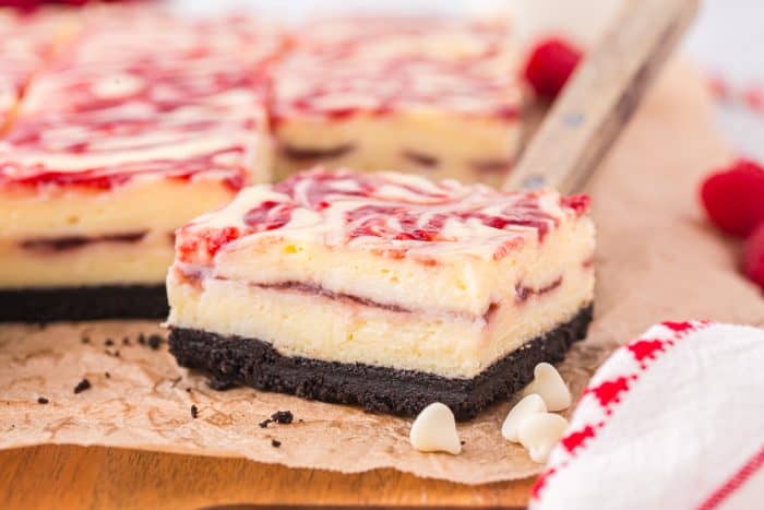 A close up of a cheesecake bar on parchment paper with white chocolate chips.