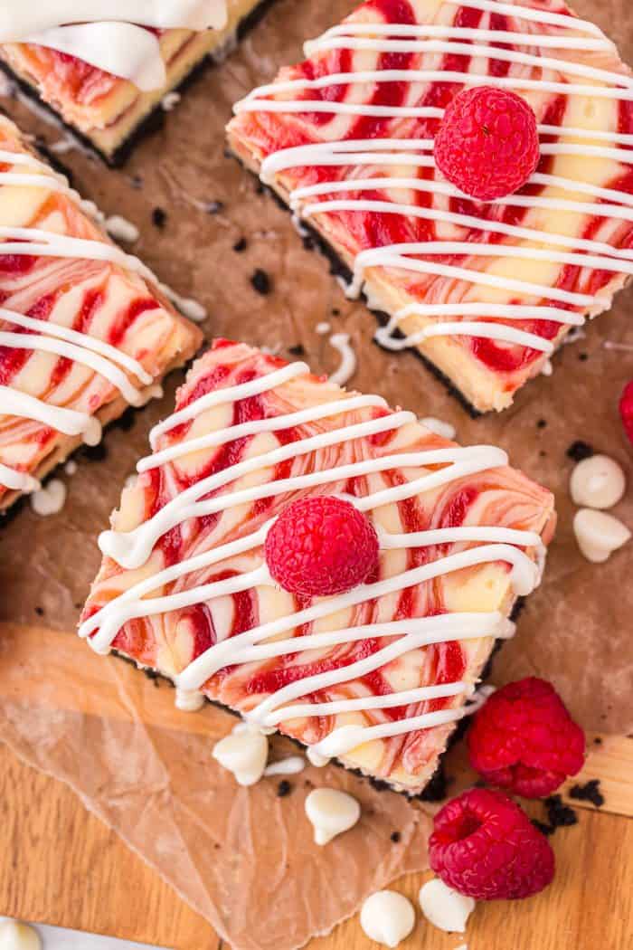 An overview of three cheesecake bars with white chocolate drizzled on parchment paper.