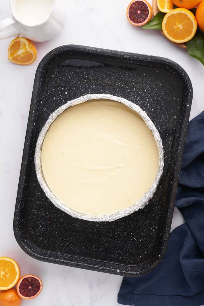 The unbaked cheesecake in the pan in a baking pan with water.