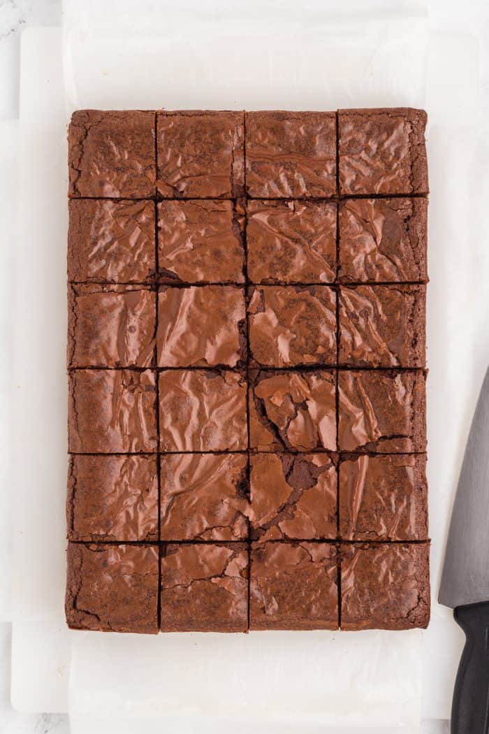 Brownies cut into squares on a cutting board with a knife.