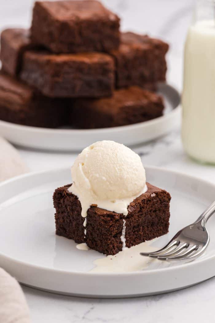 A brownie with ice cream on top with a fork on a white plate.