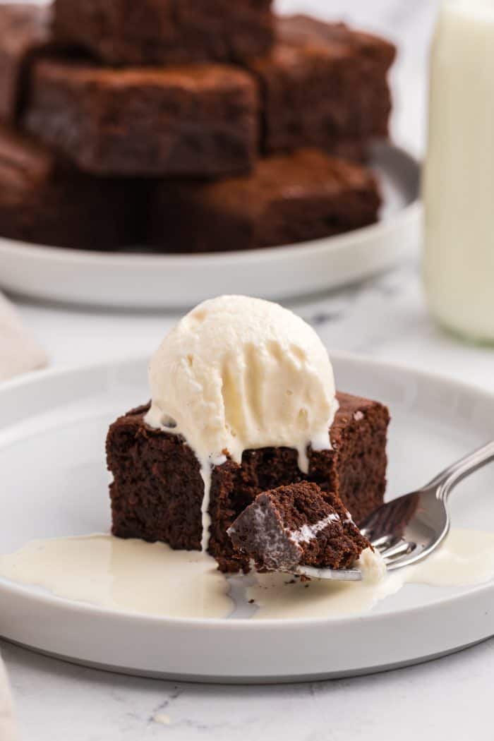 A brownie with ice cream on top with a fork on a white plate and a bite taken out of it.