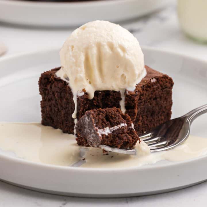 A brownie with a scoop of ice cream on it on a white plate with a fork with a little piece of brownie.