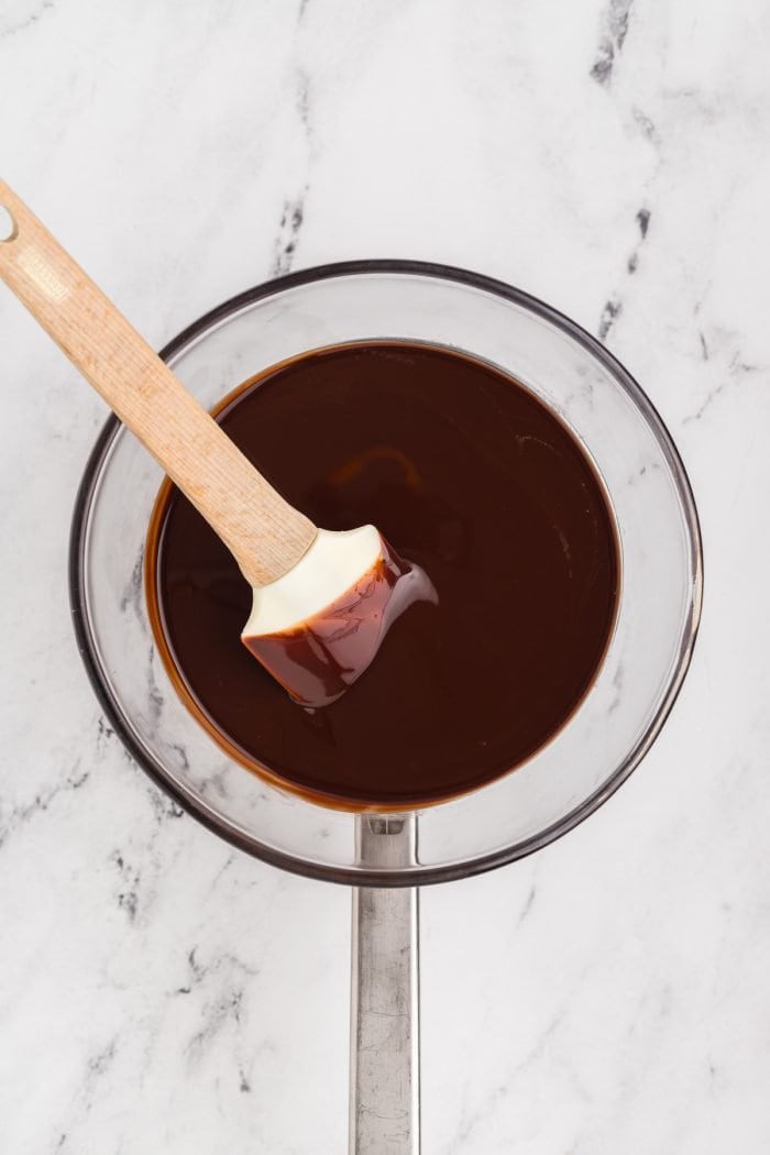 A glass bowl with chocolate melted and a spatula.