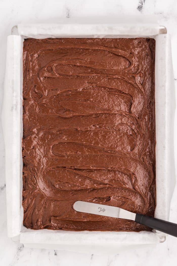 A baking pan with brownie batter being smoothed using a tool.