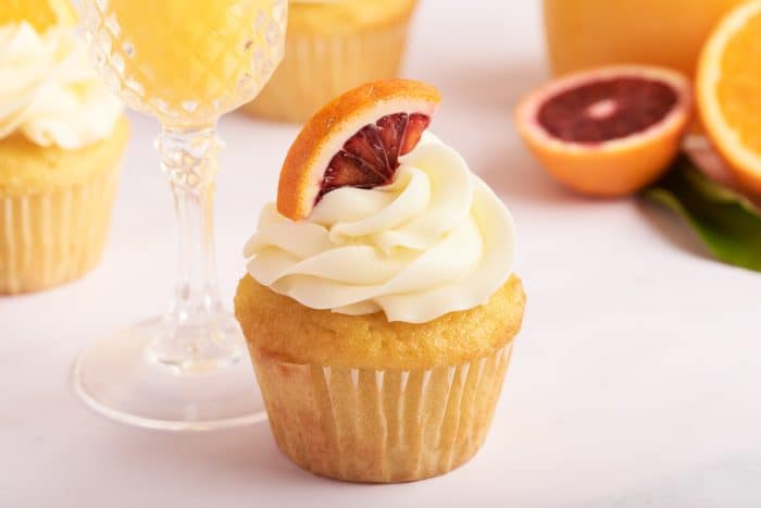 A mimosa cupcake with a glass of mimosa and a glass bottle of orange juice in the background.
