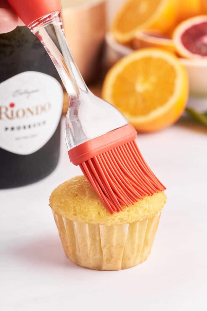 A cupcake being brushed with Prosecco syrup. 