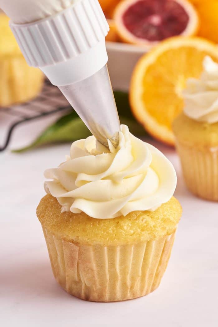 A mimosa cupcake being frosted with buttercream.