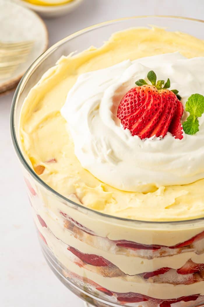 A closeup of a strawberry trifle that is garnished with whipped cream and a sliced strawberry.