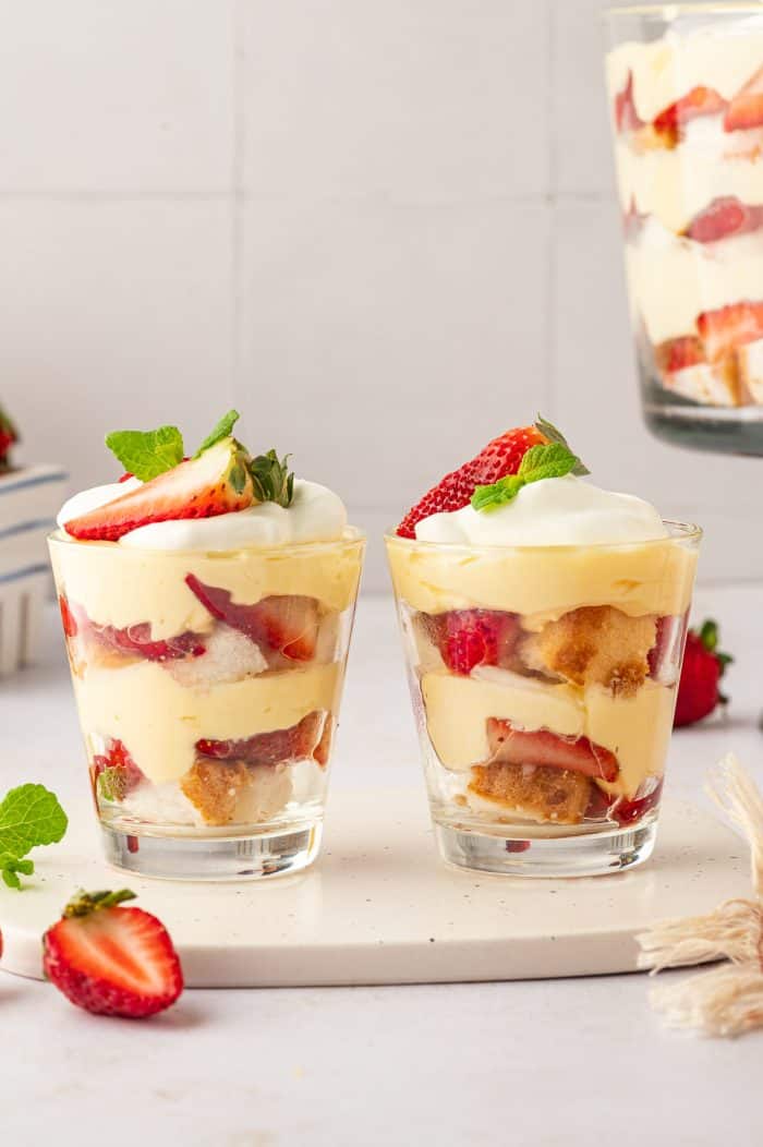 Two glass filled with strawberry trifle with strawberries in the background.