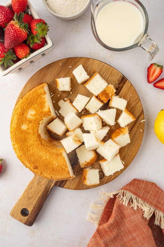 Angel food cake that is cut into cubes on a round cutting board. 