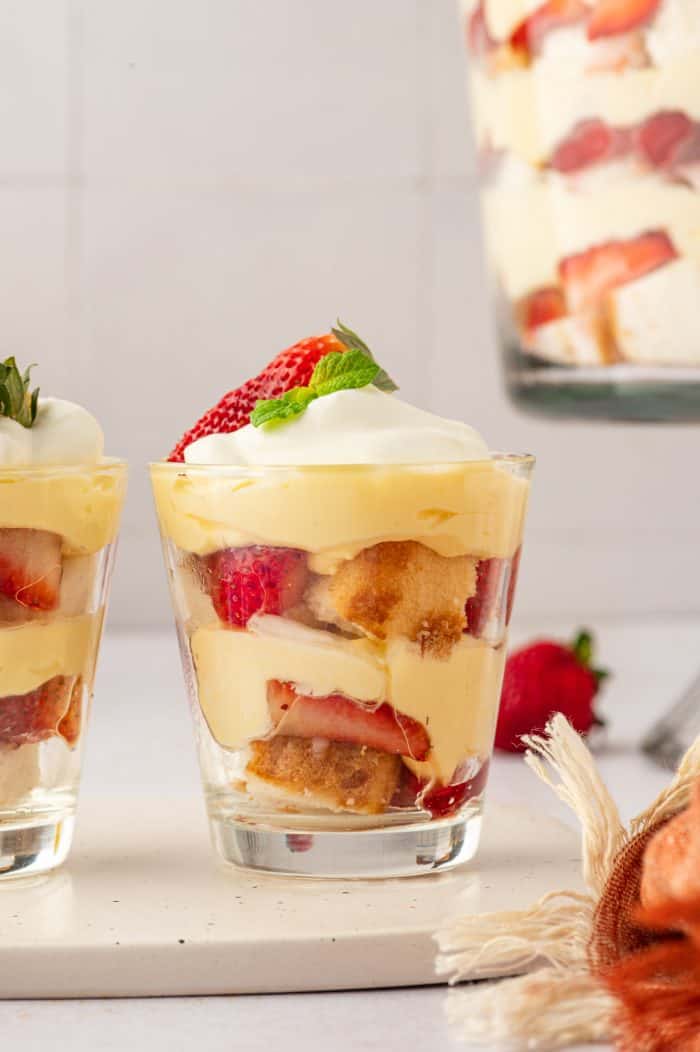 Two glass filled with strawberry trifle with strawberry trifle in the background