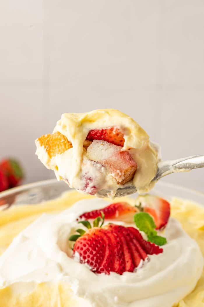 A scoop of strawberry trifle  with the whole trifle in the background.