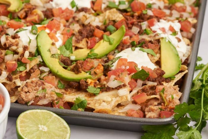 An upclose image of sheet pan nachos showing the sliced avocados and tortilla chips with melted cheese.