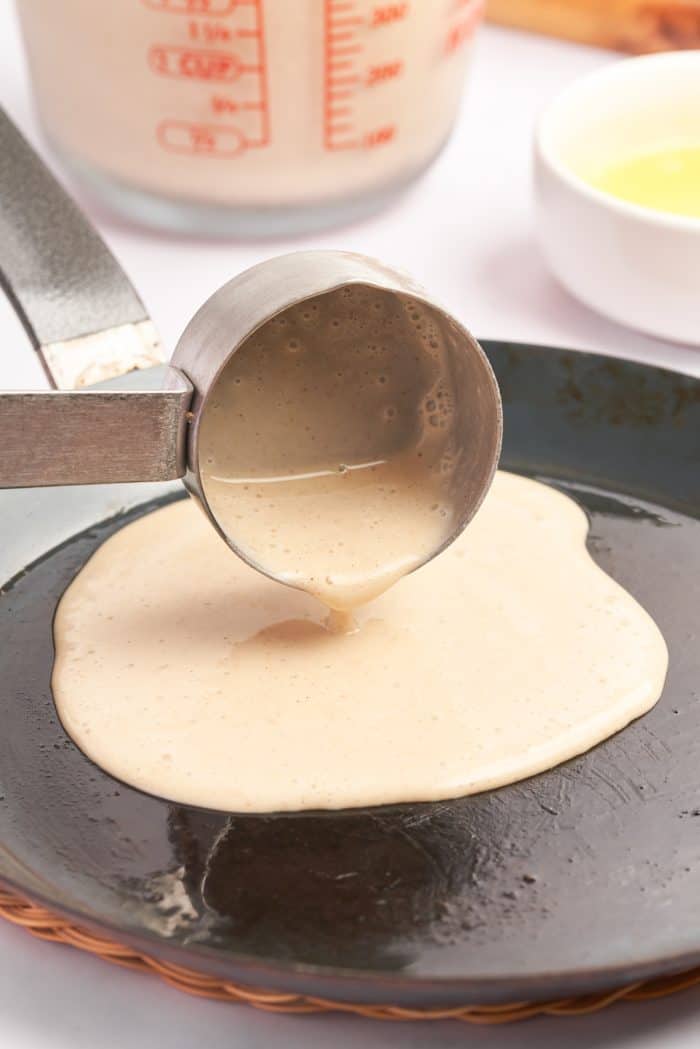 Crepe batter being poured into a hot crepe pan.