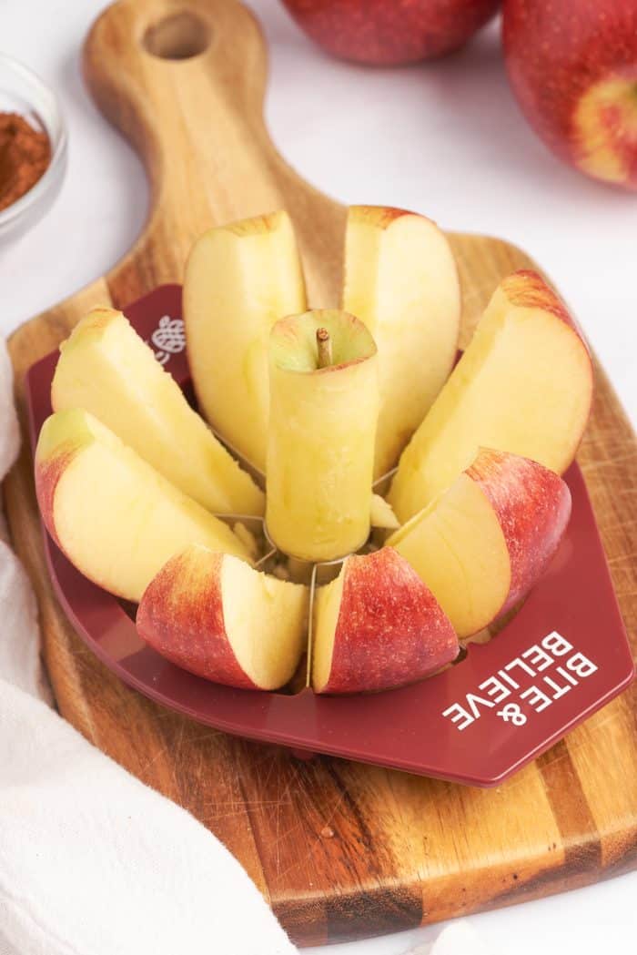 A wooden cutting board with an Envy Apples, apple slicer, slicing through an apple.