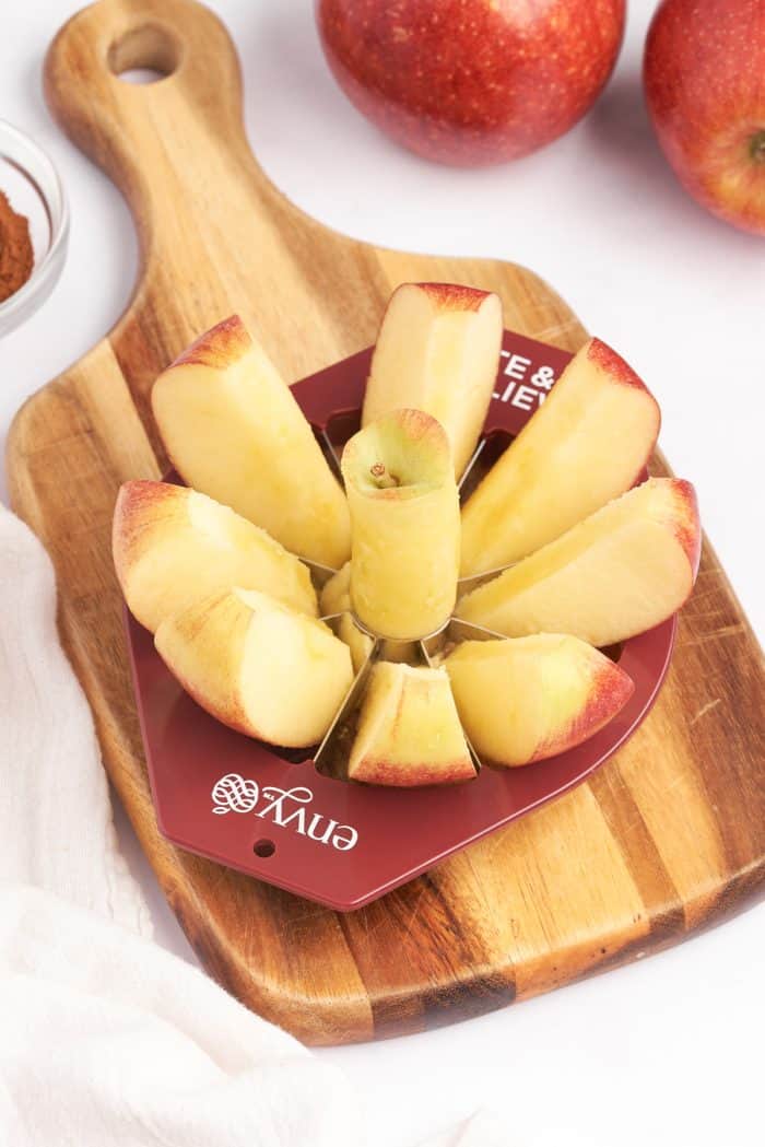 A wooden cutting board with an Envy Apples, apple slicer, slicing through an apple.