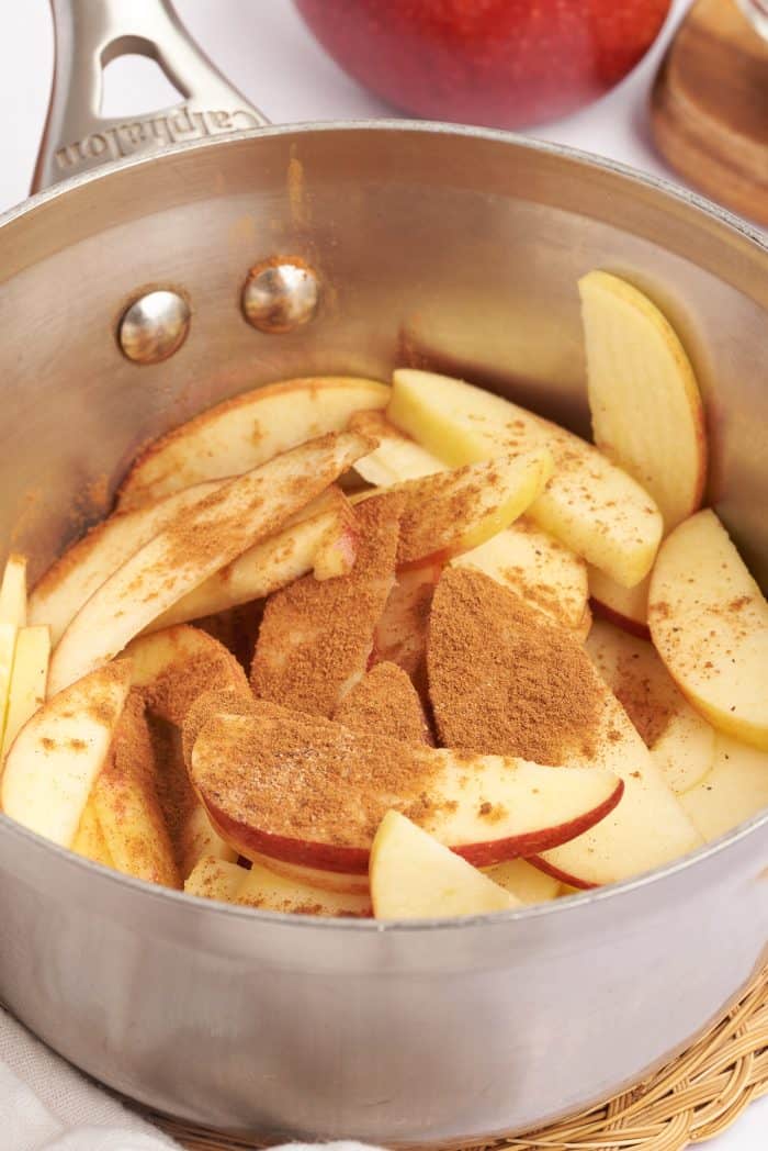 A saucepan with sliced apples, cinnamon, sugar, and lemon juice.