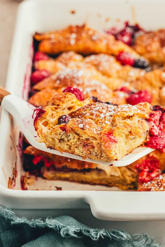 Croissant French toast bake in a white casserole dish with a spatula removing a slice of it.
