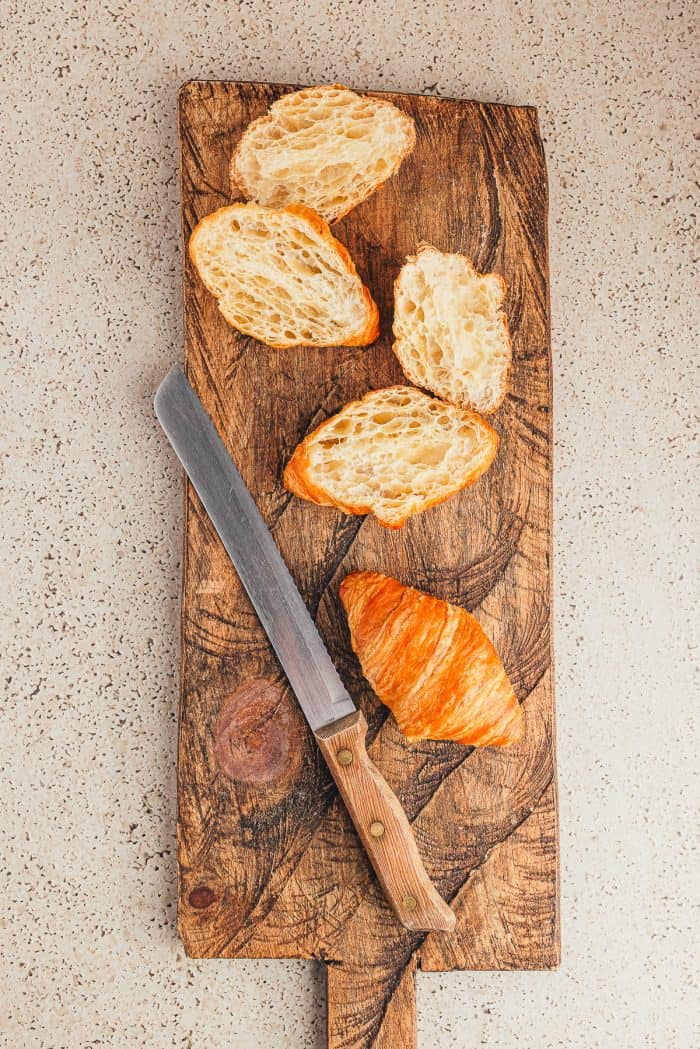 A cutting board with sliced croissants and a bread knife.