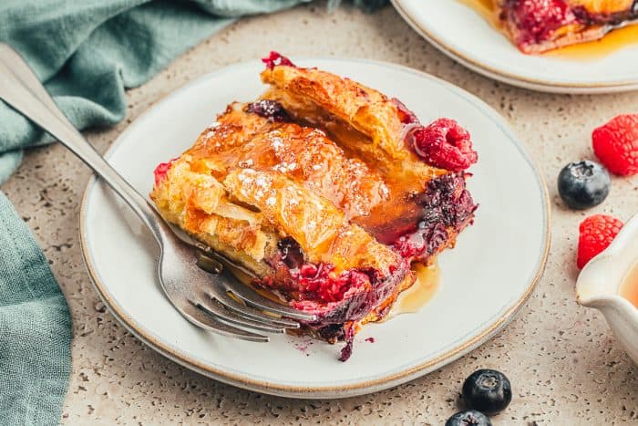 A slice of croissant French toast bake on a white plate with berries and a fork.
