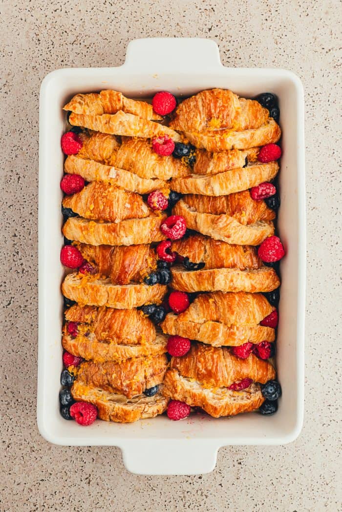 A white baking tray with sliced croissants and raspberries and blueberries.
