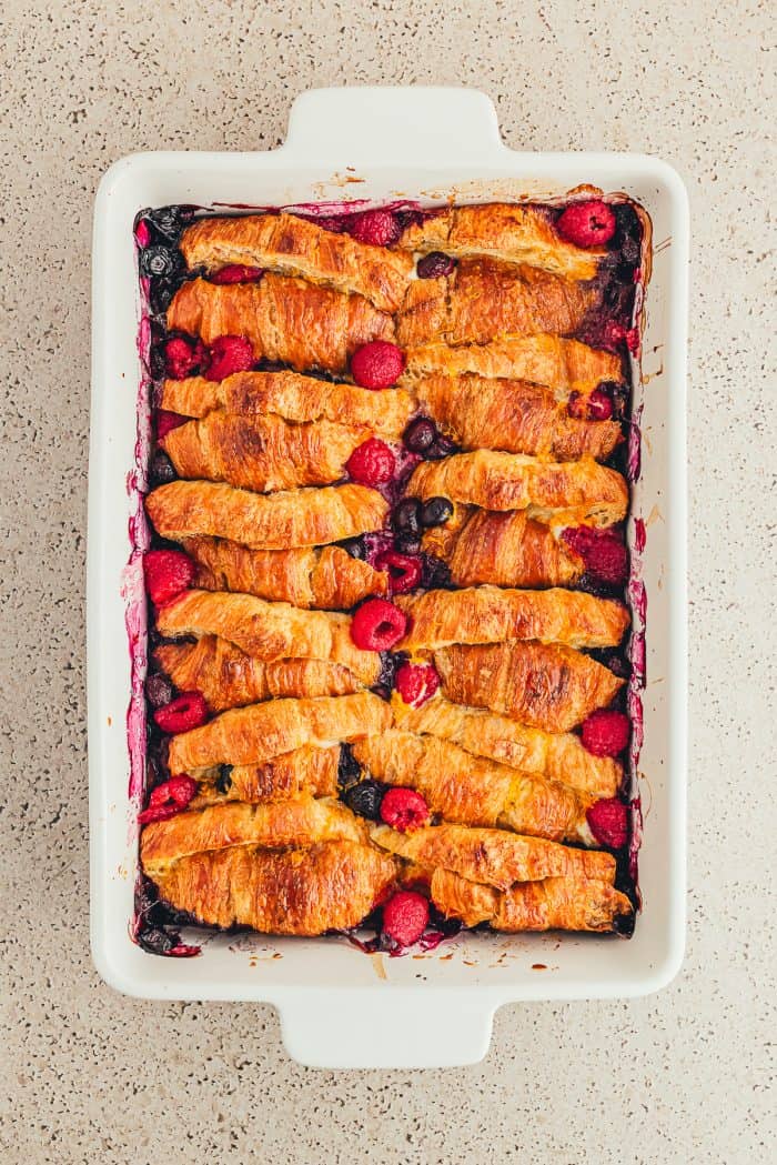 A white baking tray with baked sliced croissants French toast and raspberries and blueberries.