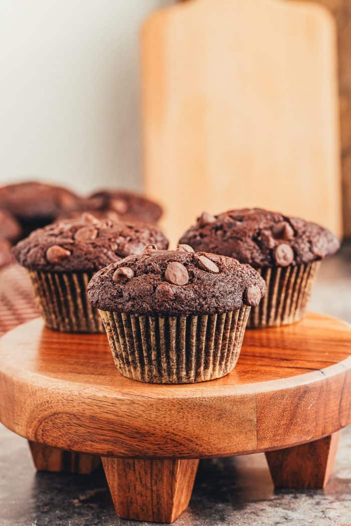 A wooden tray with three double chocolate muffins on it.