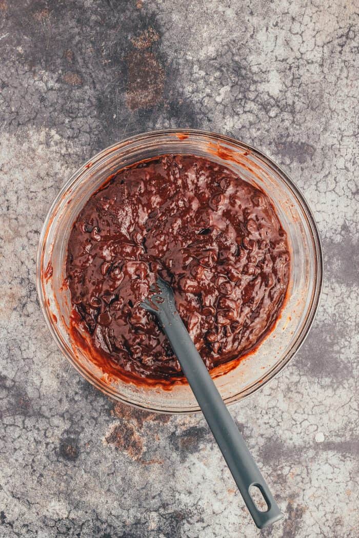 A glass bowl with the batter for double chocolate muffins and a spoon. 