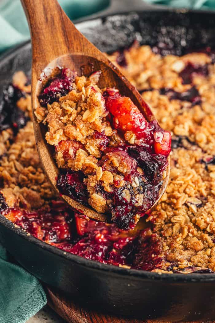 A spoon removing a scoop of blueberry and peach crumble in a cast-iron skillet.