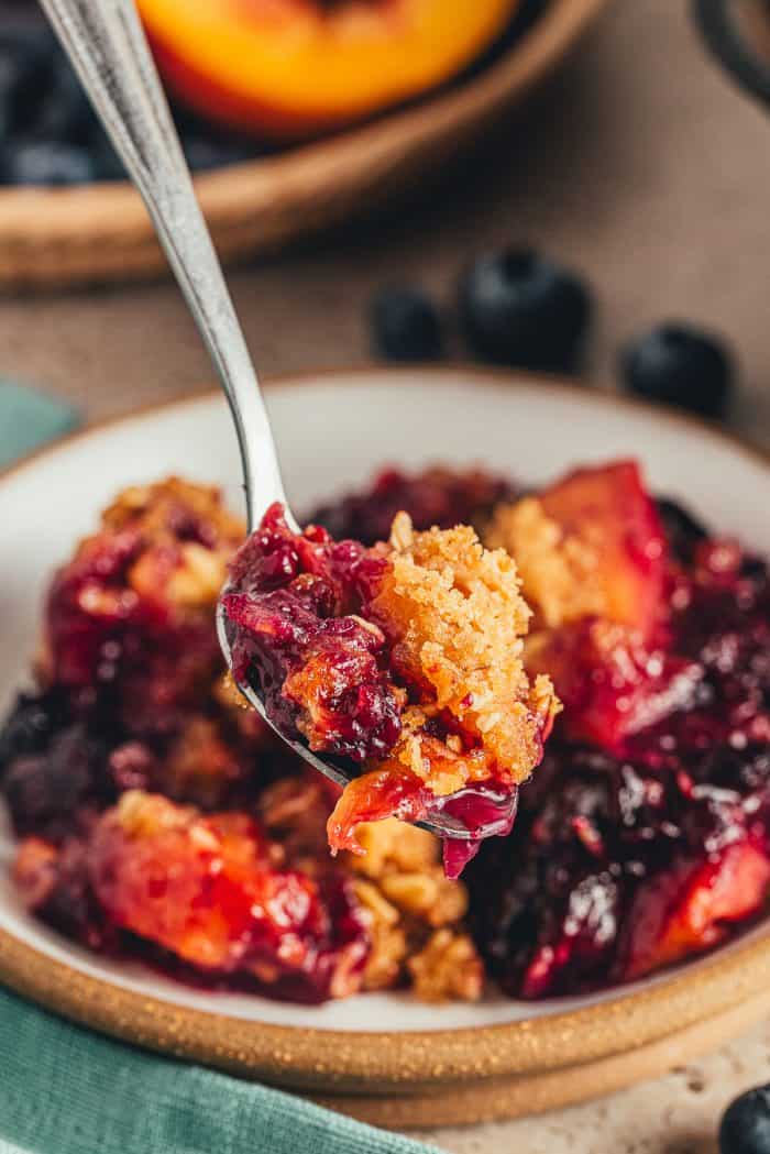 A bowl of blueberry peach crumble with a spoon.