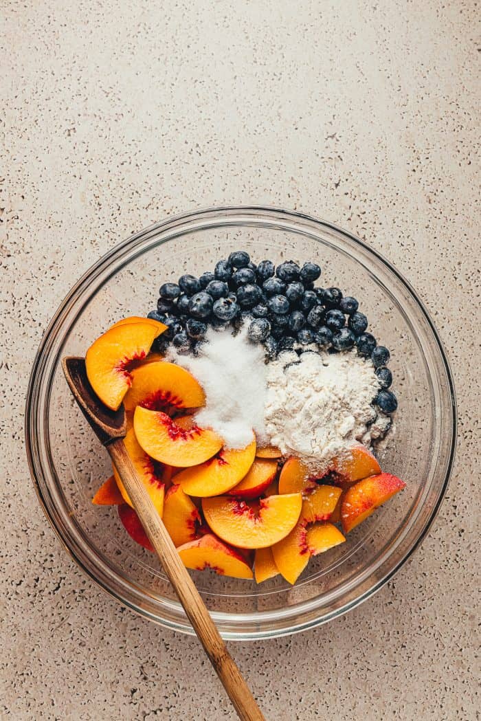 A glass bowl with fresh peaches, blueberries, and flour. 