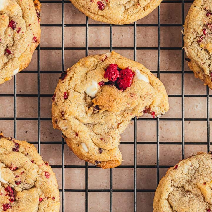 Raspberry and white chocolate cookies on a cooling rack and one cookie has a bite taken out of it.