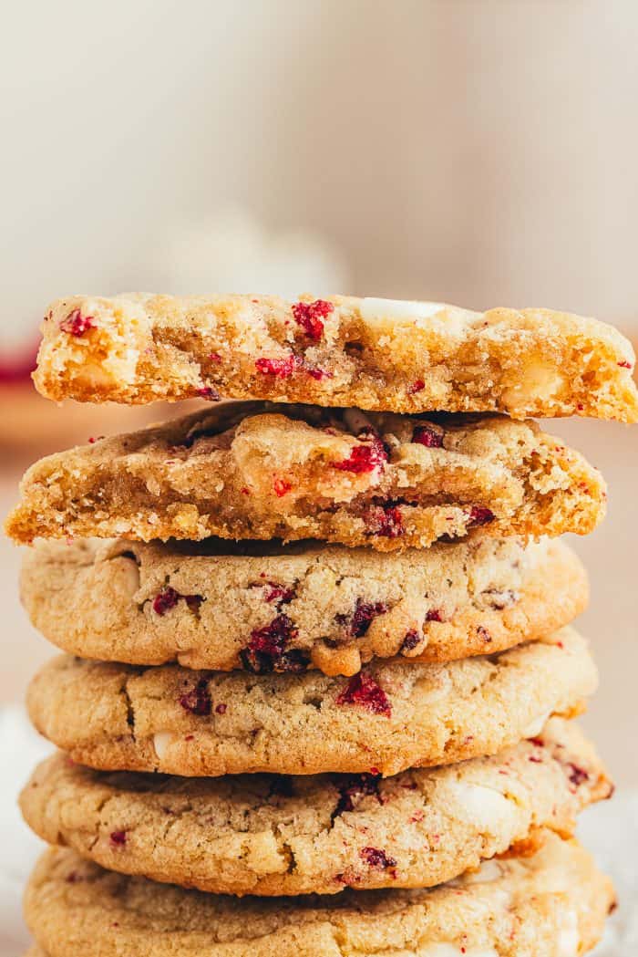 A stack of raspberry and white chocolate cookies and one cookie is broken in half.