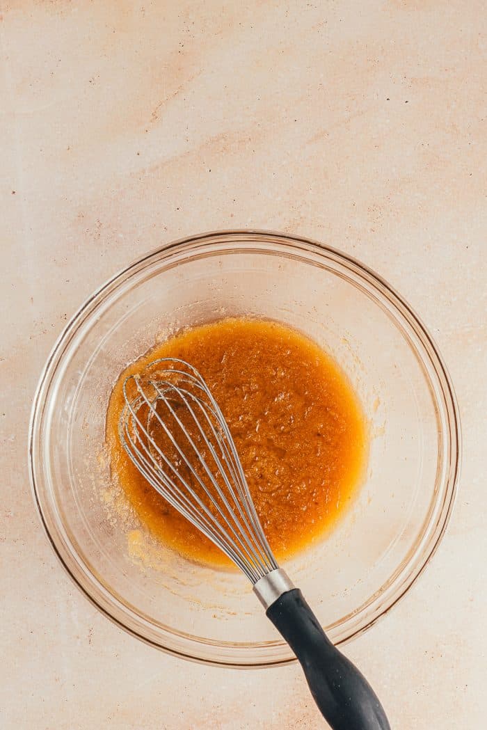 A glass bowl with melted butter and sugar and a whisk.